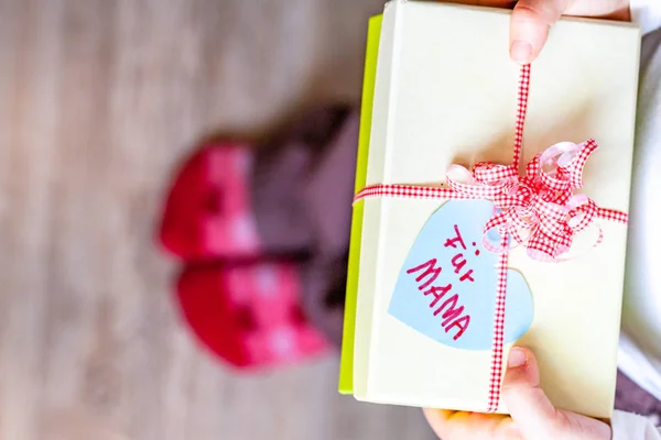 Little child holding gift box with ribbon and heart for her mum - Translation: for mum — Stock Photo, Image