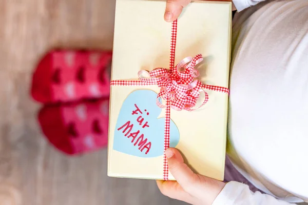 Little child holding gift box with ribbon and heart for her mum - Translation: for mum