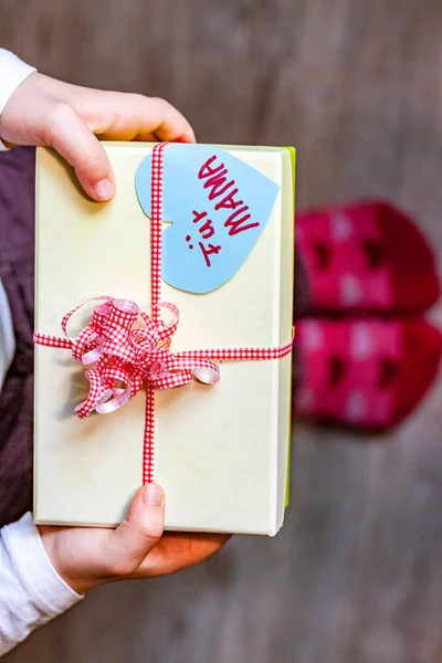 Little child holding gift box with ribbon and heart for her mum - Translation: for mum — Stock Photo, Image