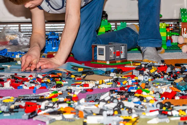 Мальчик играет с пластиковыми строительными игрушками на полу . — стоковое фото
