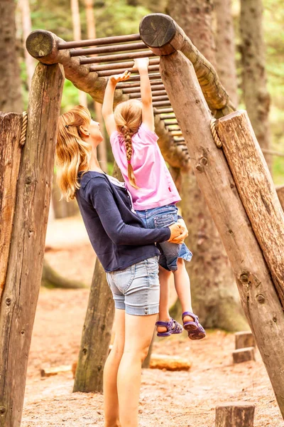Madre Apoyar a la hija en el patio de recreo con subir y colgar en una escalera — Foto de Stock