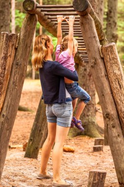 Anne tırmanma ve merdivene asılı ile oyun alanında kızı destekleyen