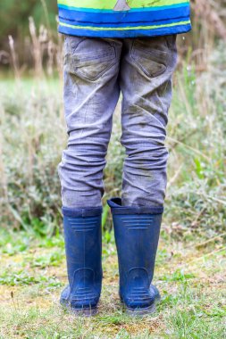 Mavi wellies giyen yeşil üzerinde duran çocuk