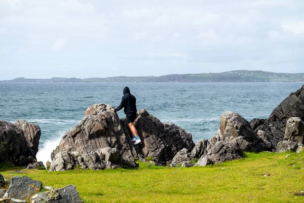 Mann, der an einem Blütenmeer mit Wasserfontänen an der wunderschönen Küste neben Carrickabraghy Castle steht - Isle of Doagh, Inishowen, County Donegal - Irland — Stockfoto