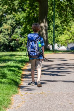 Çocuk büyük bir sırt çantasıyla parkta yürüyor.