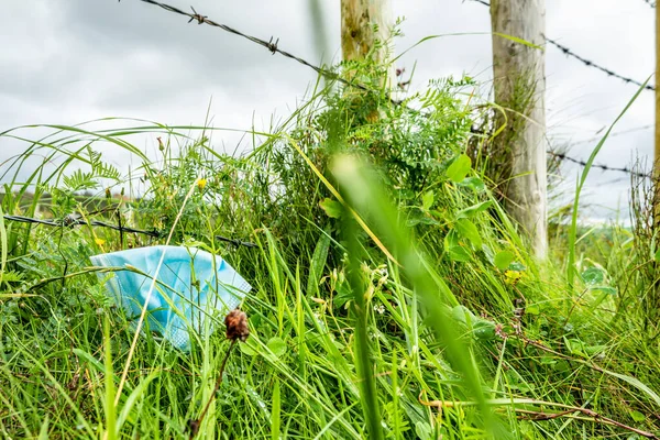 Gezichtsmasker vuilnis in het groen tijdens pandemie — Stockfoto