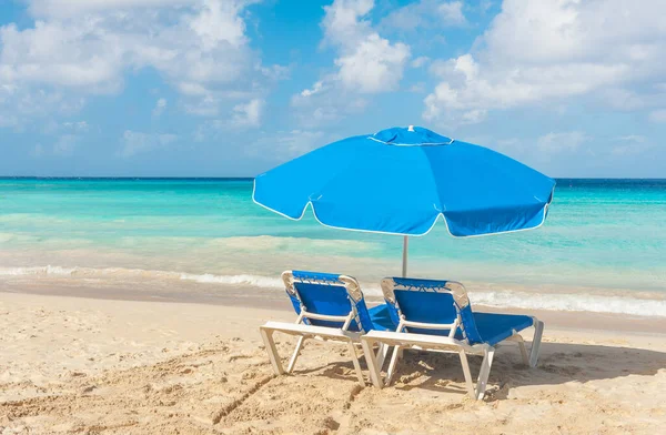 バルバドスのカリブ海のターコイズブルーの海の近くの砂浜にある2つのサンベッドと傘の青いセット — ストック写真