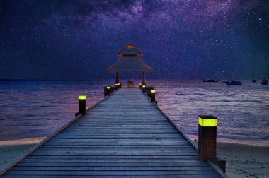 Romantik çift, Maldivler 'de deniz kenarında, yıldızların altındaki iskelede oturuyor.