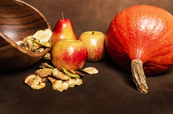 新鲜的红胡桃南瓜 罂粟头 一堆干苹果 还有两个完整的苹果和一个梨子 静止不动地生活在木碗里 秋天收获与自制水果加工的静态生活概念 褐色背景 — 图库照片