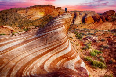 Tanımlanamayan yürüyüşçü, Nevada, ABD 'deki Fire State Park Vadisi' ndeki Wave Rock 'tan gün batımını izliyor.