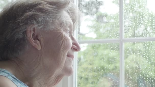 引退したシニアの白人女性の悲しみと雨の日の熟考と彼女の窓の外を見て — ストック動画