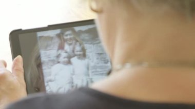 Kafkasyalı bir kadın, tablet bilgisayarındaki genç bir kadın olarak eski fotoğraflarına bakıyor.