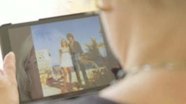 Üst düzey bir beyaz kadın kendini bir tablet bilgisayarda eski fotoğrafları bakarak yansıması 
