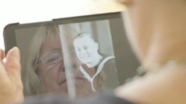Üst düzey bir beyaz kadın kendini bir tablet bilgisayarda eski fotoğrafları bakarak yansıması 