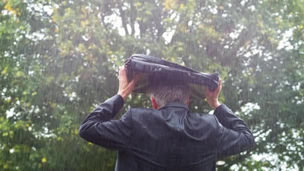 后视图的一个湿透的白种商人躲在他的包在雨中 — 图库视频影像