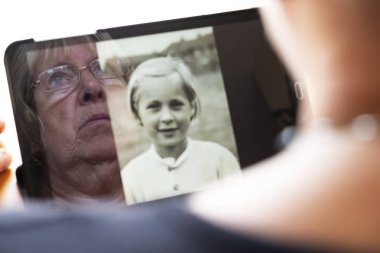 Yaşlanma süreci nostalji ve çocukluk temalarının zıttı olan tablet bilgisayar temalı eski fotoğraflarına bakan beyaz kadın.