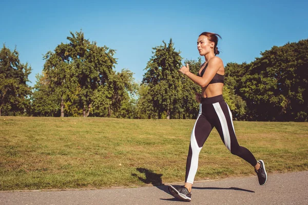 beautiful woman in black white leggings and sportive top running in park
