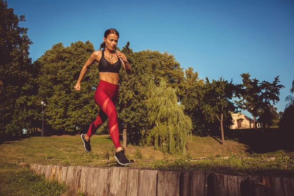 caucasian woman in red leggings and sportive top running and jumping in park