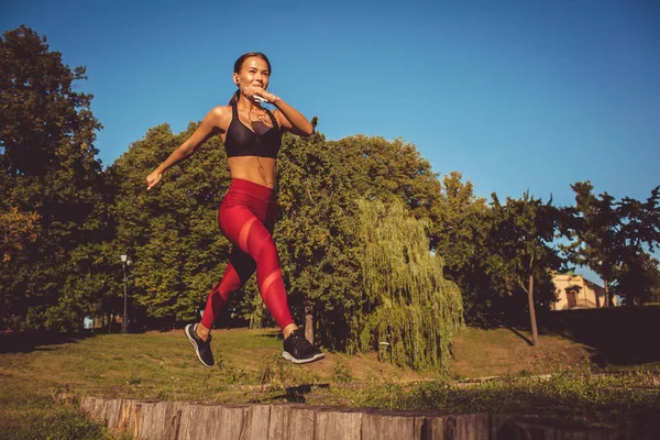 caucasian woman in red leggings and sportive top running and jumping in park