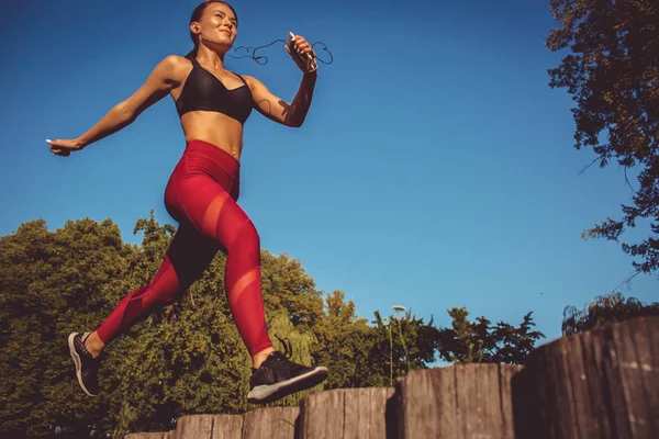 caucasian woman in red leggings and sportive top running and jumping in park