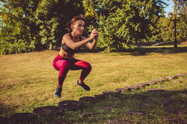 woman in red leggings and sportive top doing squats in park meadow