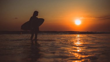 deniz suyundaki surfboard ile yürüyüş ve günbatımı ve tatil keyfini sörfçü kadın