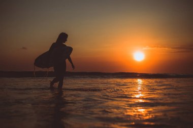 deniz suyundaki surfboard ile yürüyüş ve günbatımı ve tatil keyfini sörfçü kadın