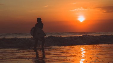 deniz suyundaki surfboard ile yürüyüş ve gökyüzü günbatımı, turuncu güneşte zevk sörfçü kadın 