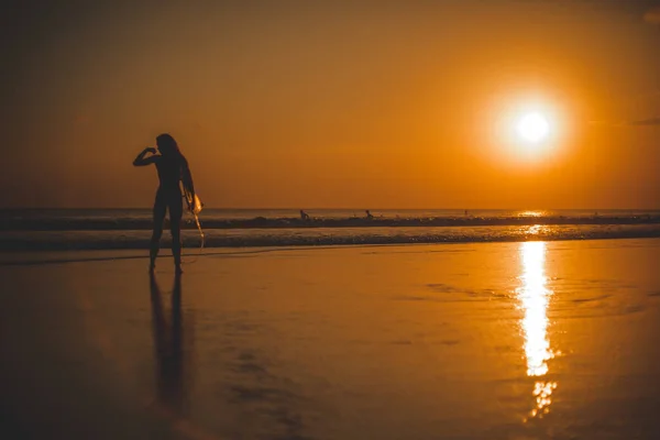 back view of woman with surfboard in sea, sunset time