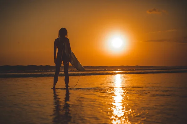 back view, full length of surfer woman standing with surfboard in sea