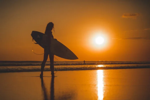 back view, full length of surfer woman standing with surfboard in sea