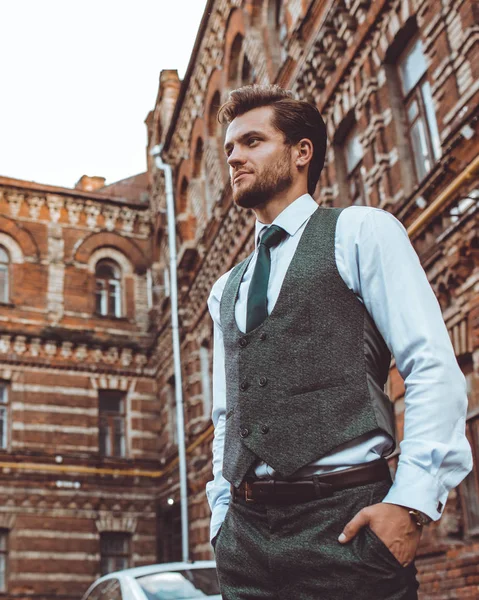 stock image businessman in suit vest posing at brick building, holding hands in pockets 