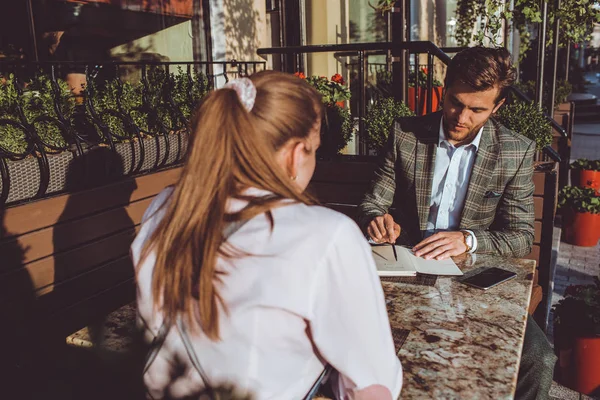 handsome Caucasian man sitting outdoors in cafe at meeting with woman