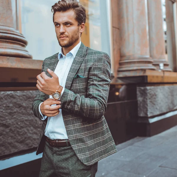 serious elegant Caucasian man in tweed suit jacket walking in street and adjusting sleeve