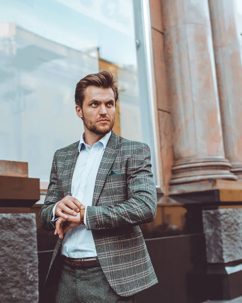 handsome Caucasian businessman in tweed suit jacket outdoors at hotel building with columns