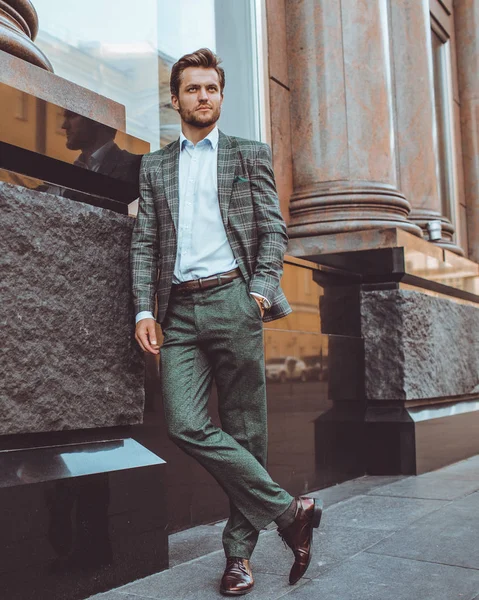 full length of stylish Caucasian gentleman in tweed suit jacket posing at building in street