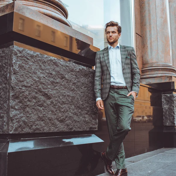 full length of stylish Caucasian gentleman in tweed suit jacket posing at building in street