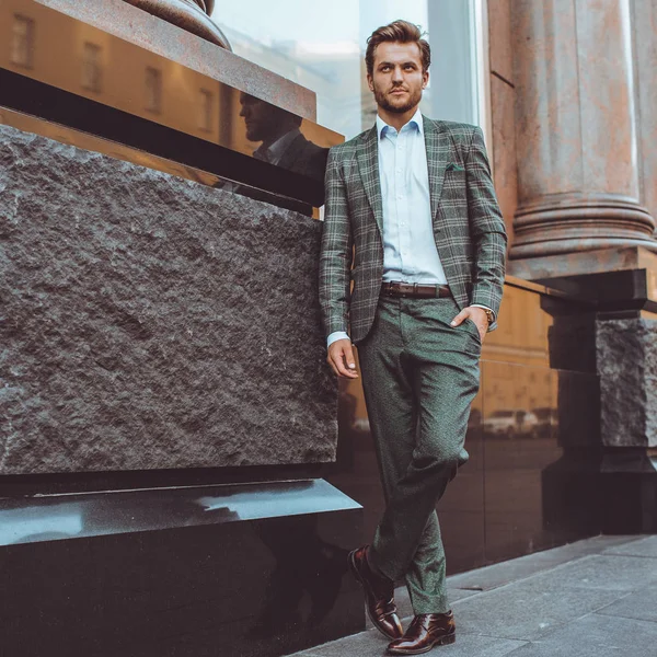full length of stylish Caucasian gentleman in tweed suit jacket posing at building in street