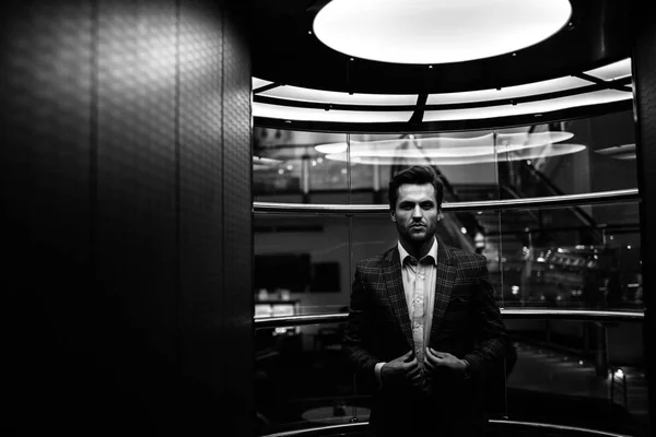 handsome Caucasian gentleman adjusting tweed suit jacket and standing in glass elevator