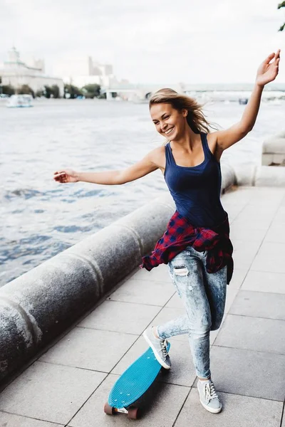笑う金髪女性が川でスケート ボードを持つポーズの全長 — ストック写真