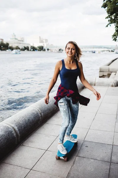 full length of happy blonde woman riding on skateboard at river