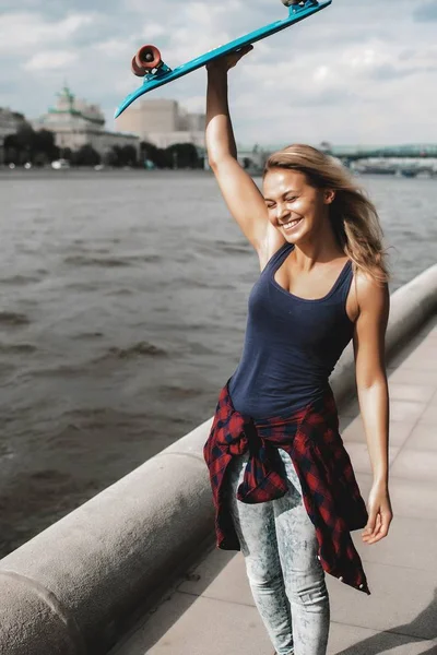 スケート ボードの頭の上を押しながら川を歩いて目を閉じて金髪女性を笑顔 — ストック写真