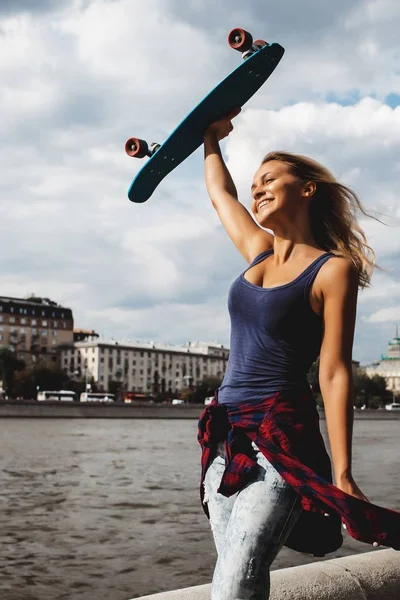 Sonriente Mujer Rubia Sosteniendo Monopatín Sobre Cabeza Caminando Río —  Fotos de Stock