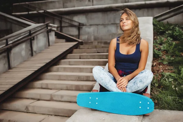 屋外の階段に座っている青いスケート ボードと美しい金髪流行に敏感なティーンエイ ジャーの女の子 — ストック写真