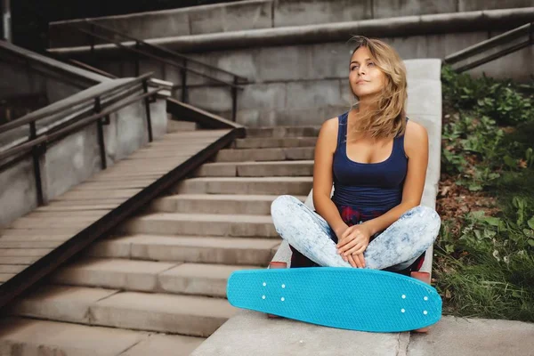 屋外の階段に座っている青いスケート ボードと美しいブロンド十代の若者スケーター — ストック写真