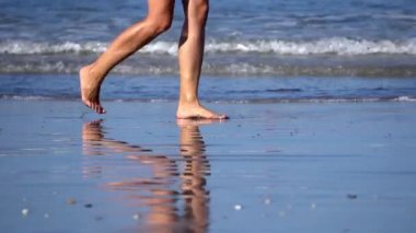 Güneşli bir günde, Endonezya, Bali 'de kumsalda çıplak ayakla yürüyen birinin kırpılmış görüntüsü.