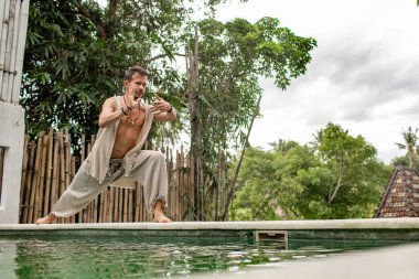 Şaman tropikal bahçede havuz kenarında vücut egzersizleri yapıyor ve pratik yapıyor.
