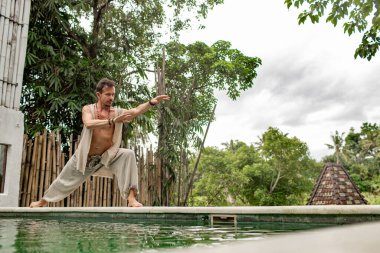 Şaman tropikal bahçede havuz kenarında vücut egzersizleri yapıyor ve pratik yapıyor.