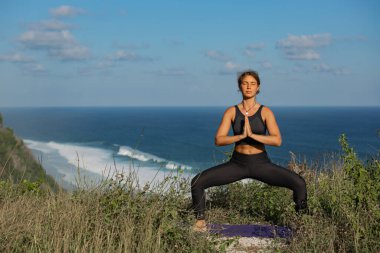 Okyanus kenarında yoga yapan sakin genç bir kadın.