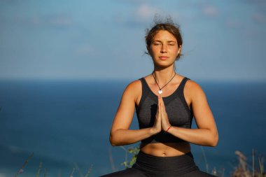 Okyanus kenarında yoga yapan sakin genç bir kadın.